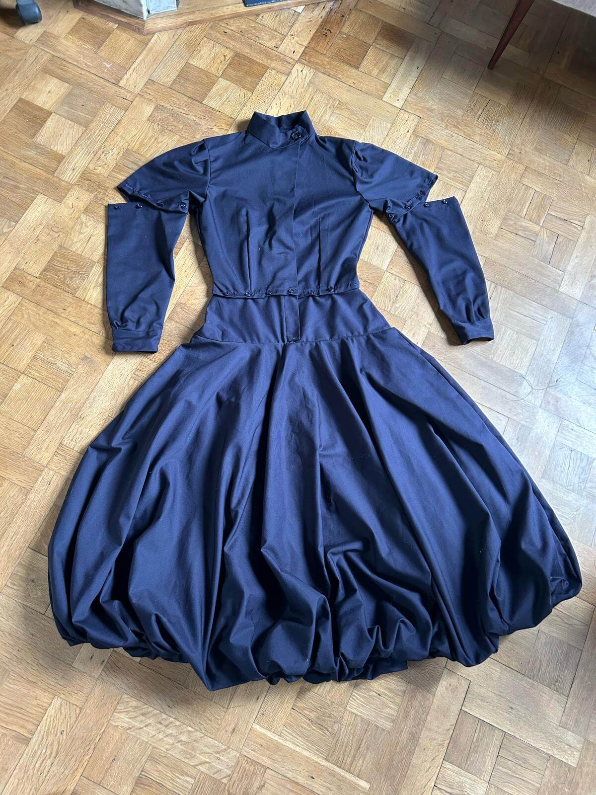 Complete navy modular dress laid flat on wooden floor showing all components: top, detachable sleeves, and balloon skirt
